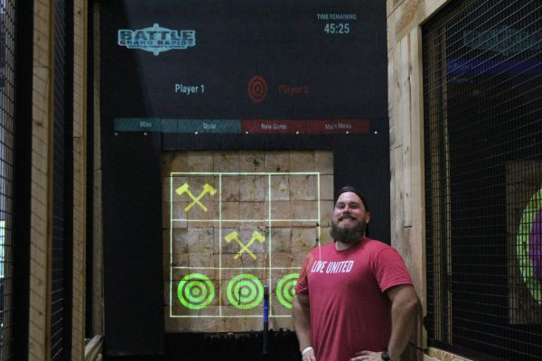 man in red shirt proudly standing in front of axe throwing at corporate event venue in grand rapids